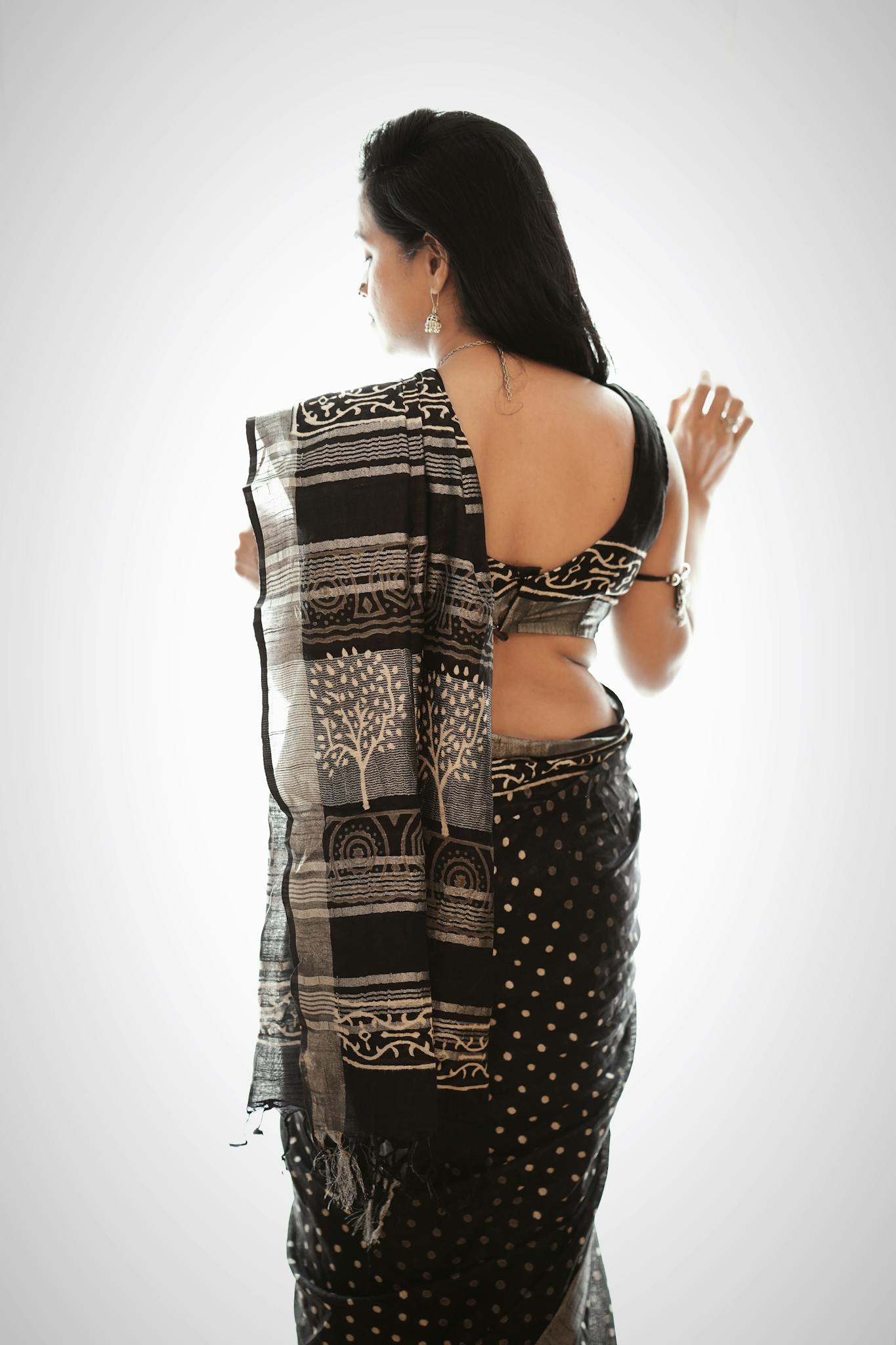 A woman wearing a traditional black saree with intricate patterns, standing gracefully.