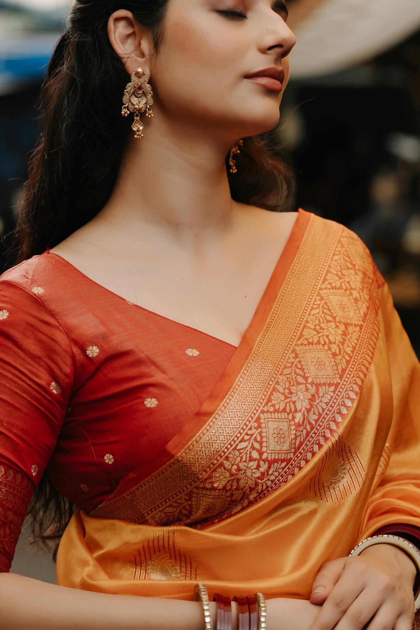 A woman wearing a traditional orange and red saree, adorned with intricate gold jewelry, expressing cultural elegance.